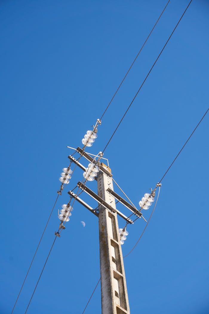 A towering utility pole with cables and insulators against a bright, clear blue sky.