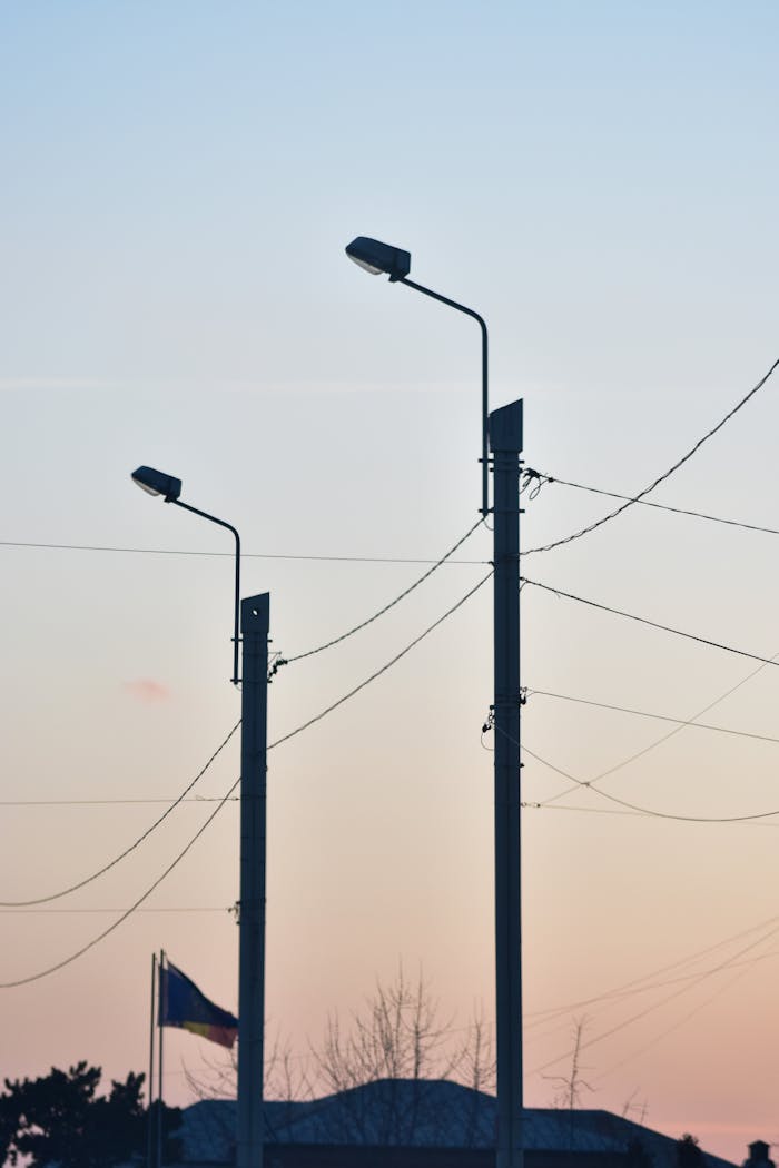 Silhouette of street lamps and electric poles against a sunset sky.