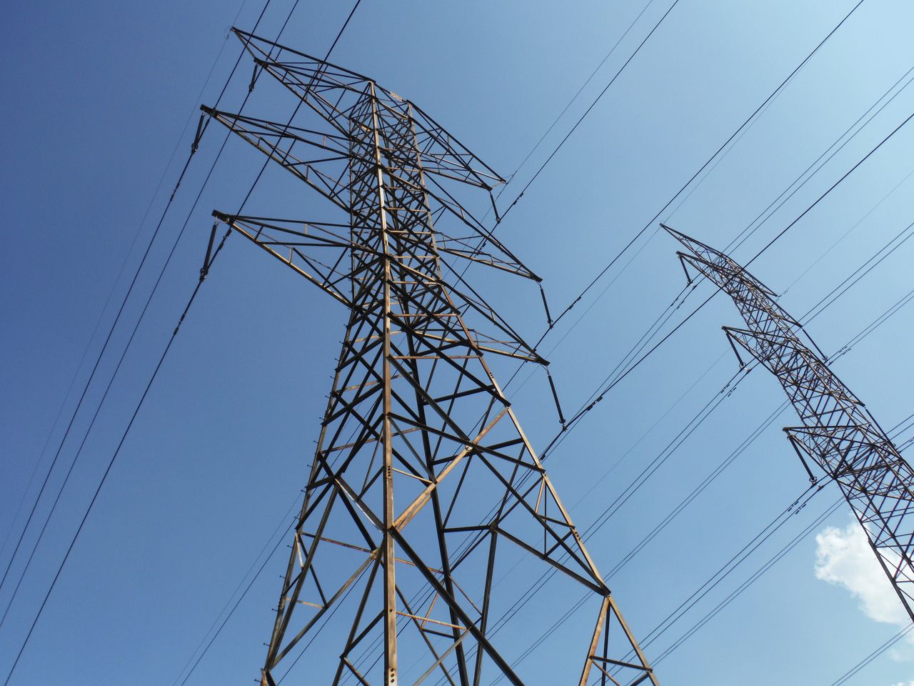 our-mission Low angle view of towering electrical transmission lines and pylons under a clear blue sky, conveying energy and electricity concepts.