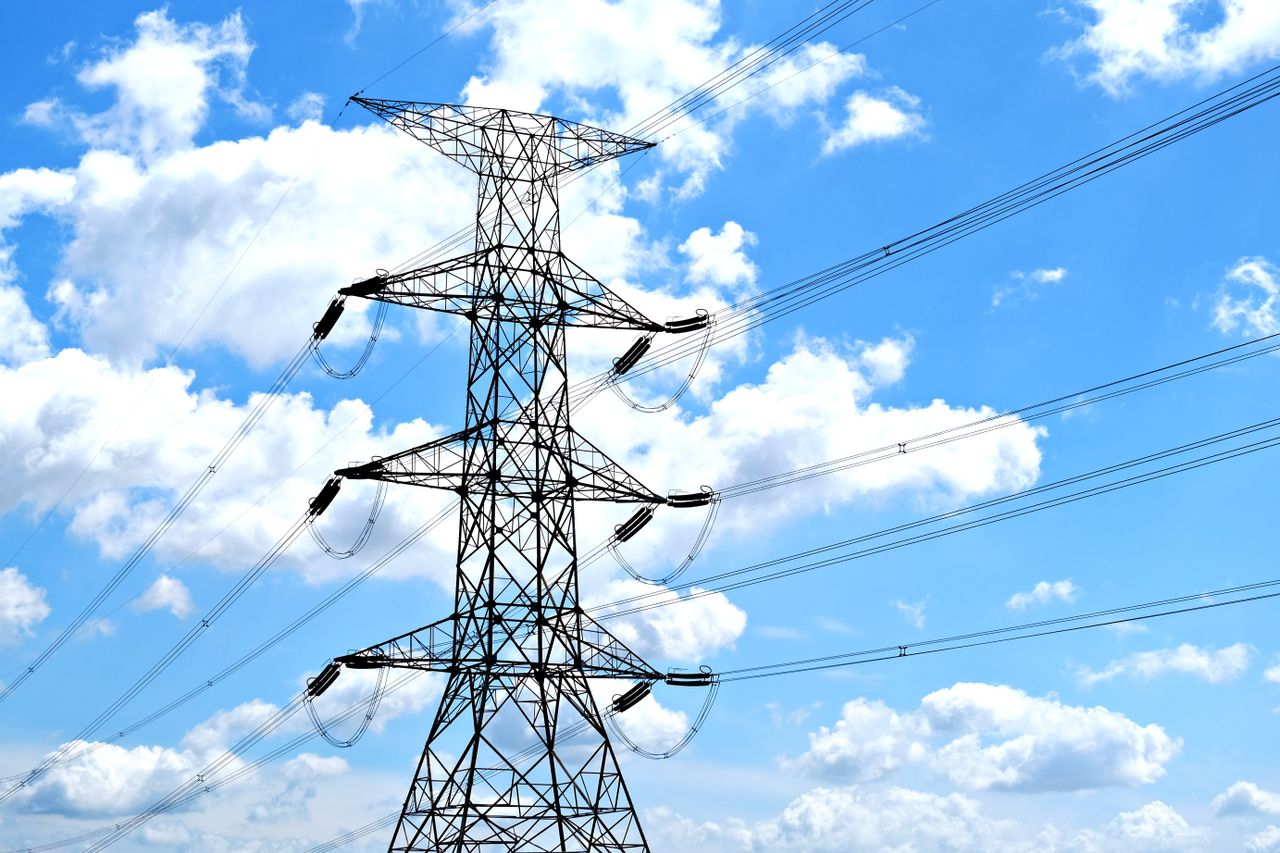 who-we-are Electricity pylon with high voltage lines set against a vibrant blue sky with clouds.